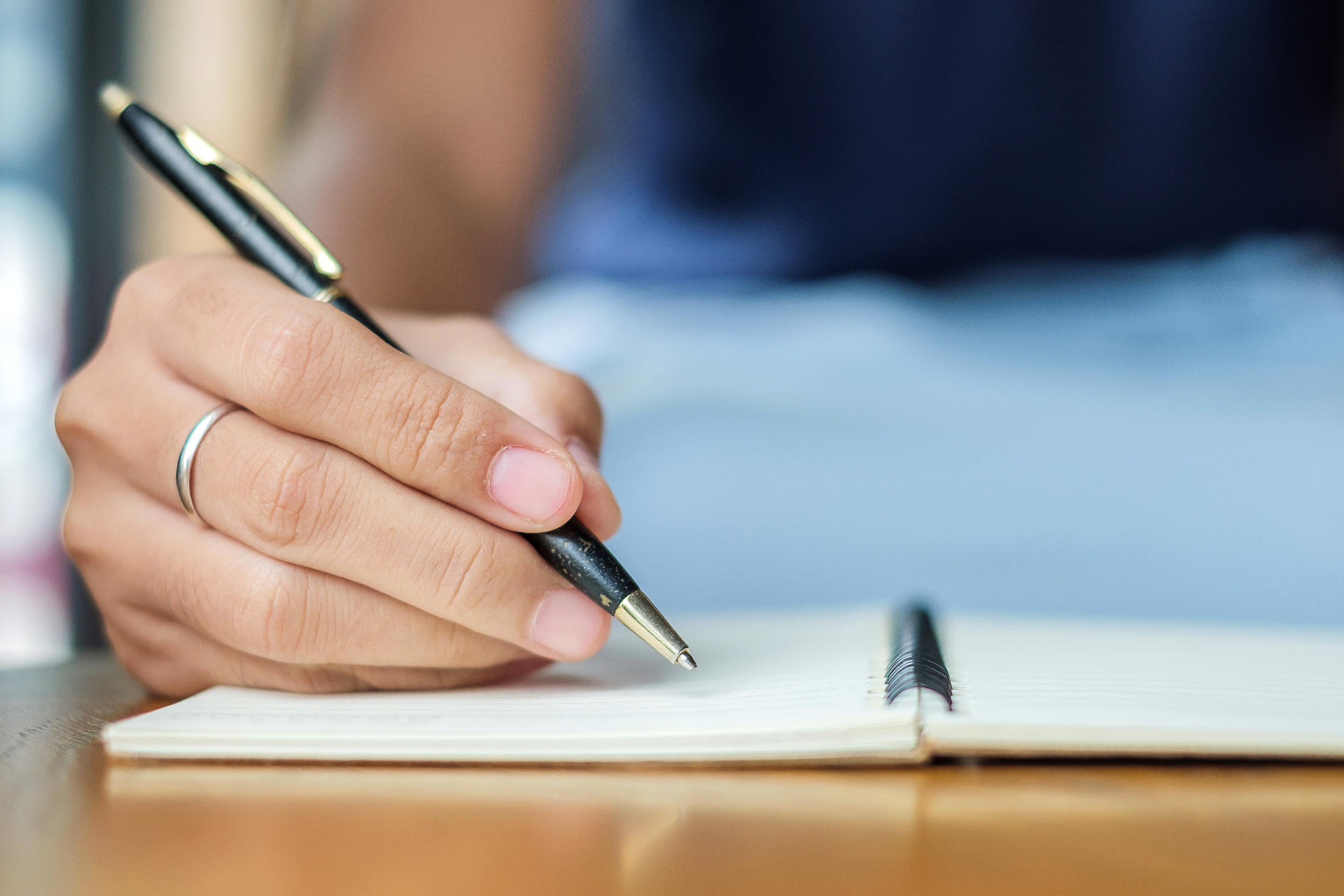 Hand holding a black pen, ready to write in an open notebook.