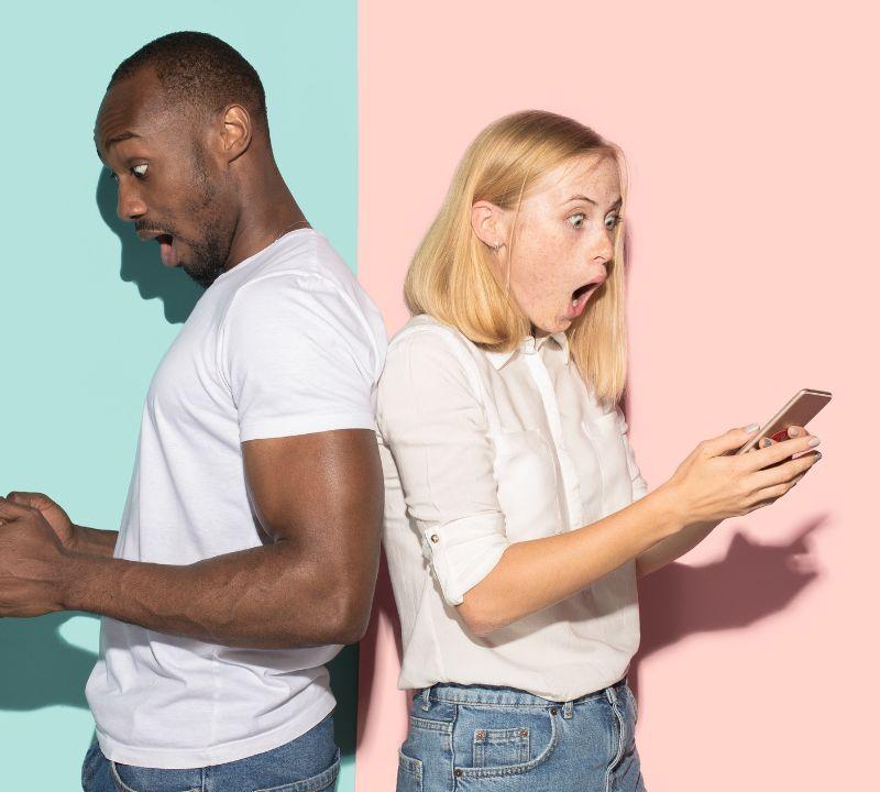 Man and woman seated back to back, each looking at their phone in surprise, comparing a custom coach website to a generic template Man and woman seated back to back, each looking at their phone in surprise, comparing a custom coach website to a generic template