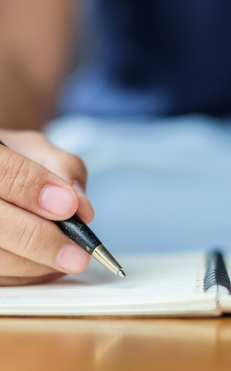 Coach's hand holding a black pen over an open notebook, drafting website copy that books more coaching clients Coach's hand holding a black pen over an open notebook, drafting website copy that books more coaching clients